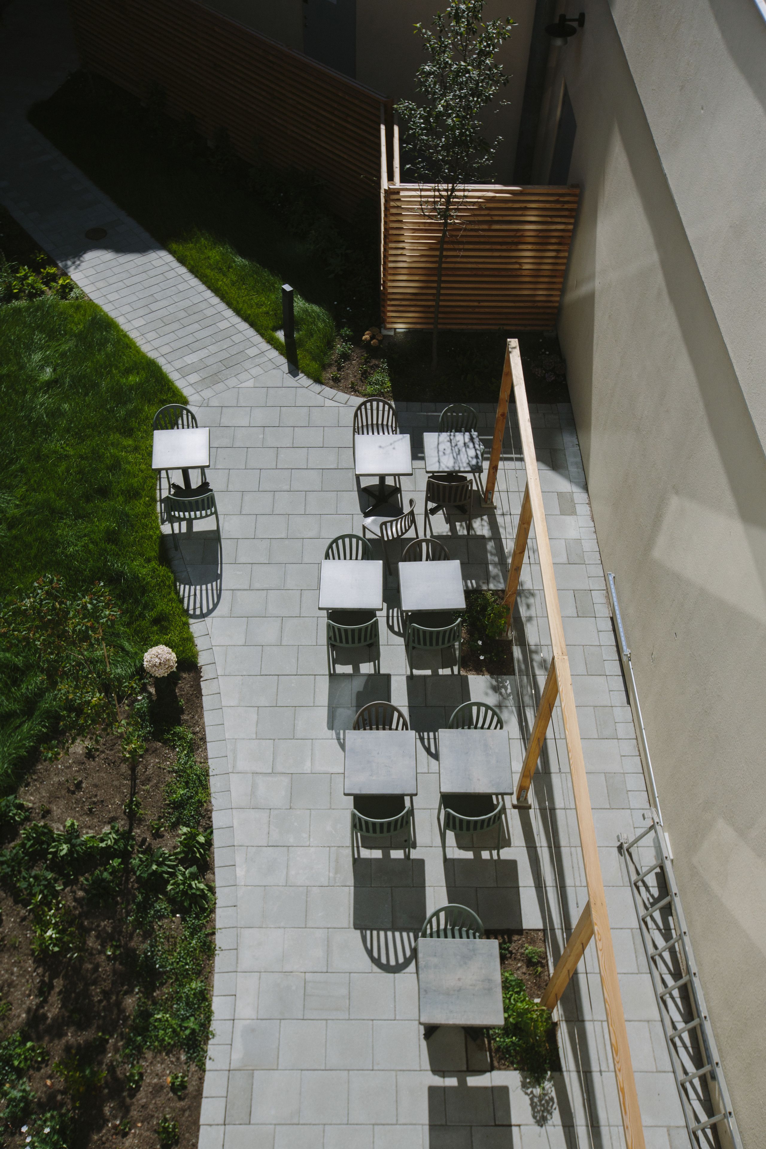 An outdoor patio with multiple tables and chairs, surrounded by a low wooden fence and a paved walkway.