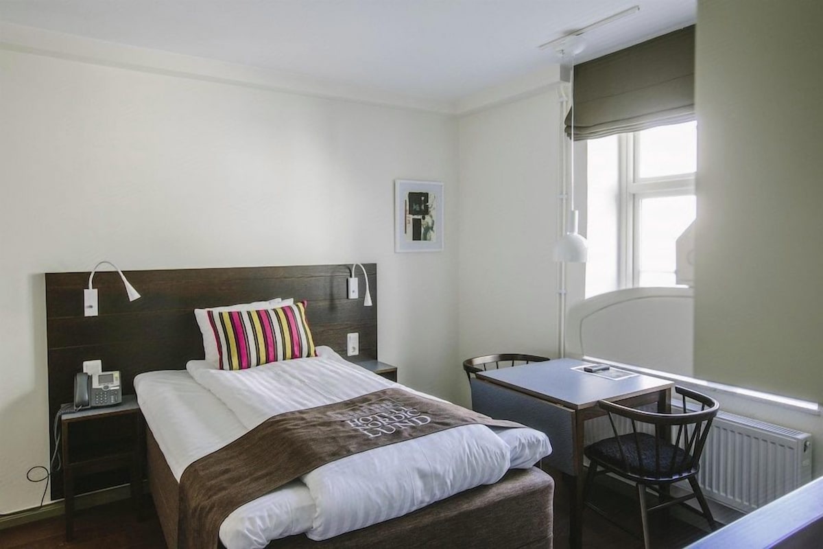 Una habitación de hotel con cama, mesita de noche, silla y ventana.