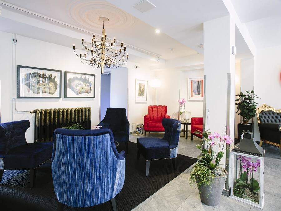 A modern hotel lobby with a chandelier, framed artwork, plush seating, and a potted plant.