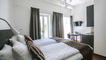 Una habitación de hotel moderna con una cama bien hecha, un escritorio con silla, un televisor y un ventanal con cortinas.