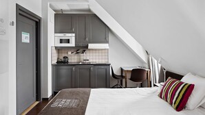 Habitación de hotel compacta con kitchenette, una cama con almohada a rayas y un escritorio con silla.