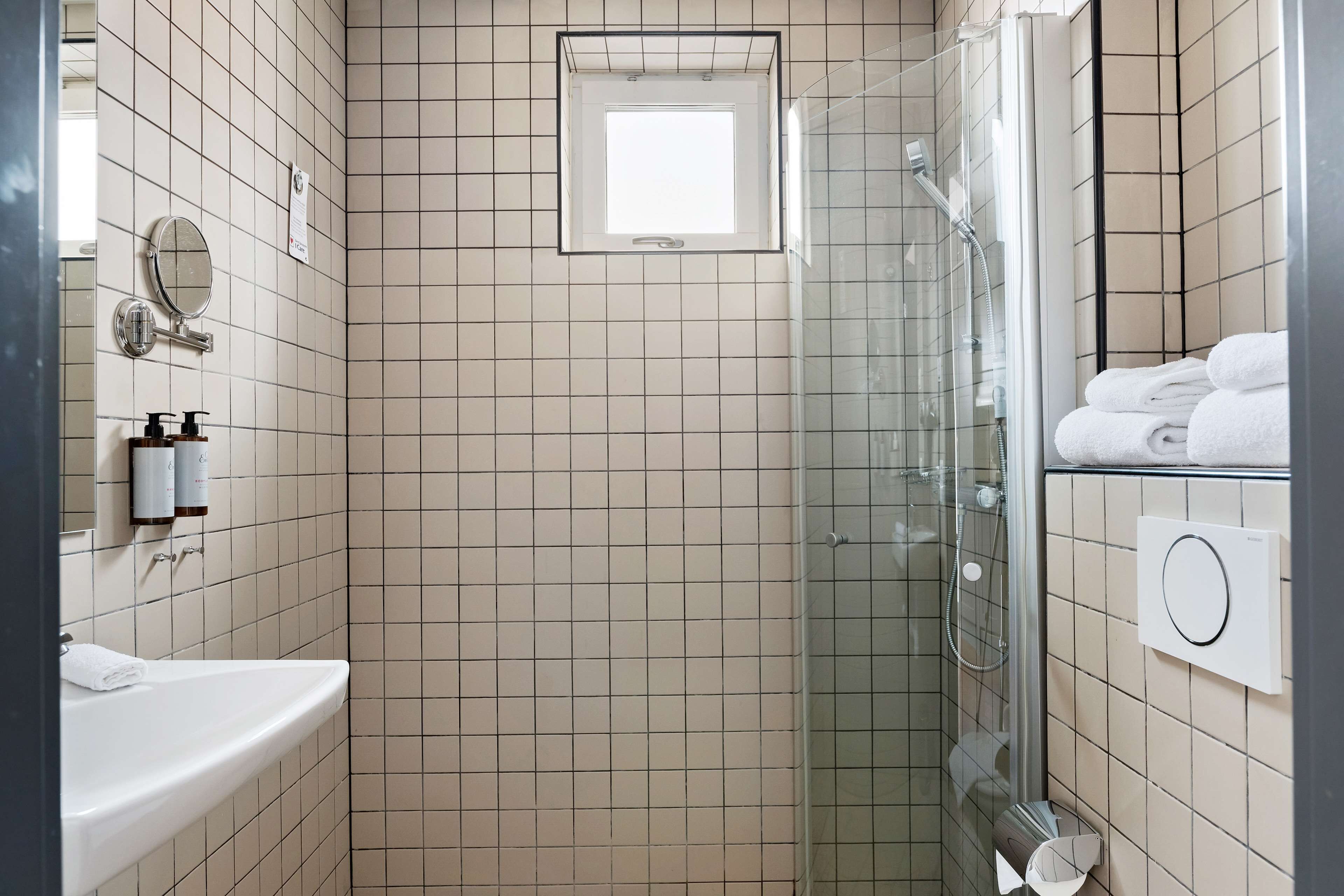 Un baño con ducha de vidrio, lavamanos, espejo y perchero para toallas.