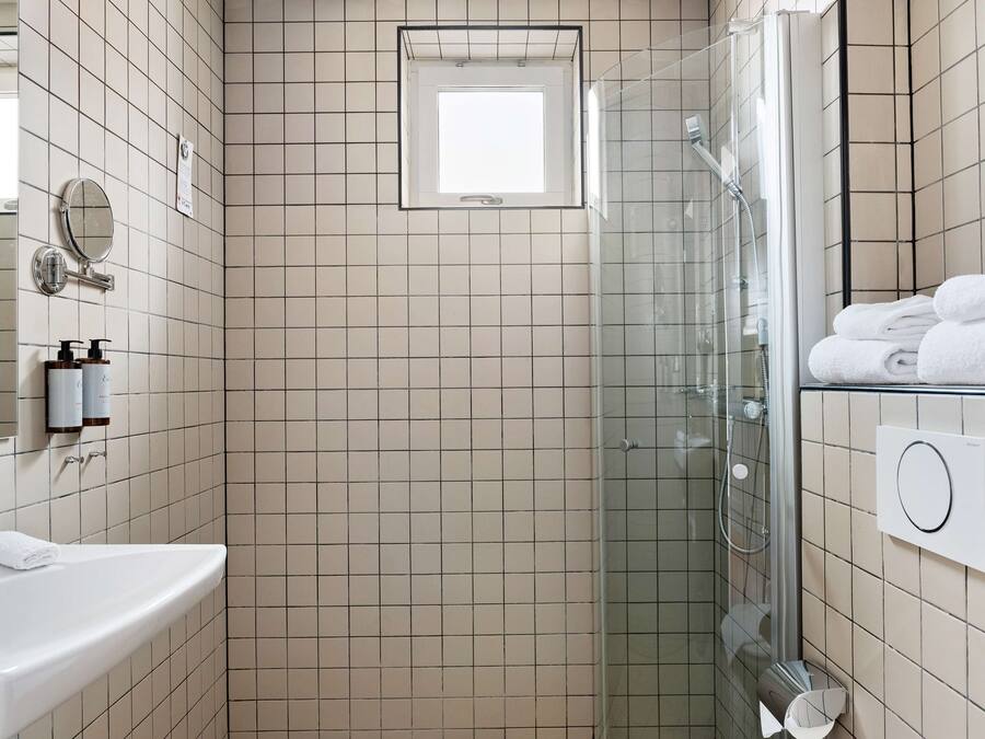 Un baño con ducha de vidrio, lavamanos, espejo y perchero para toallas.