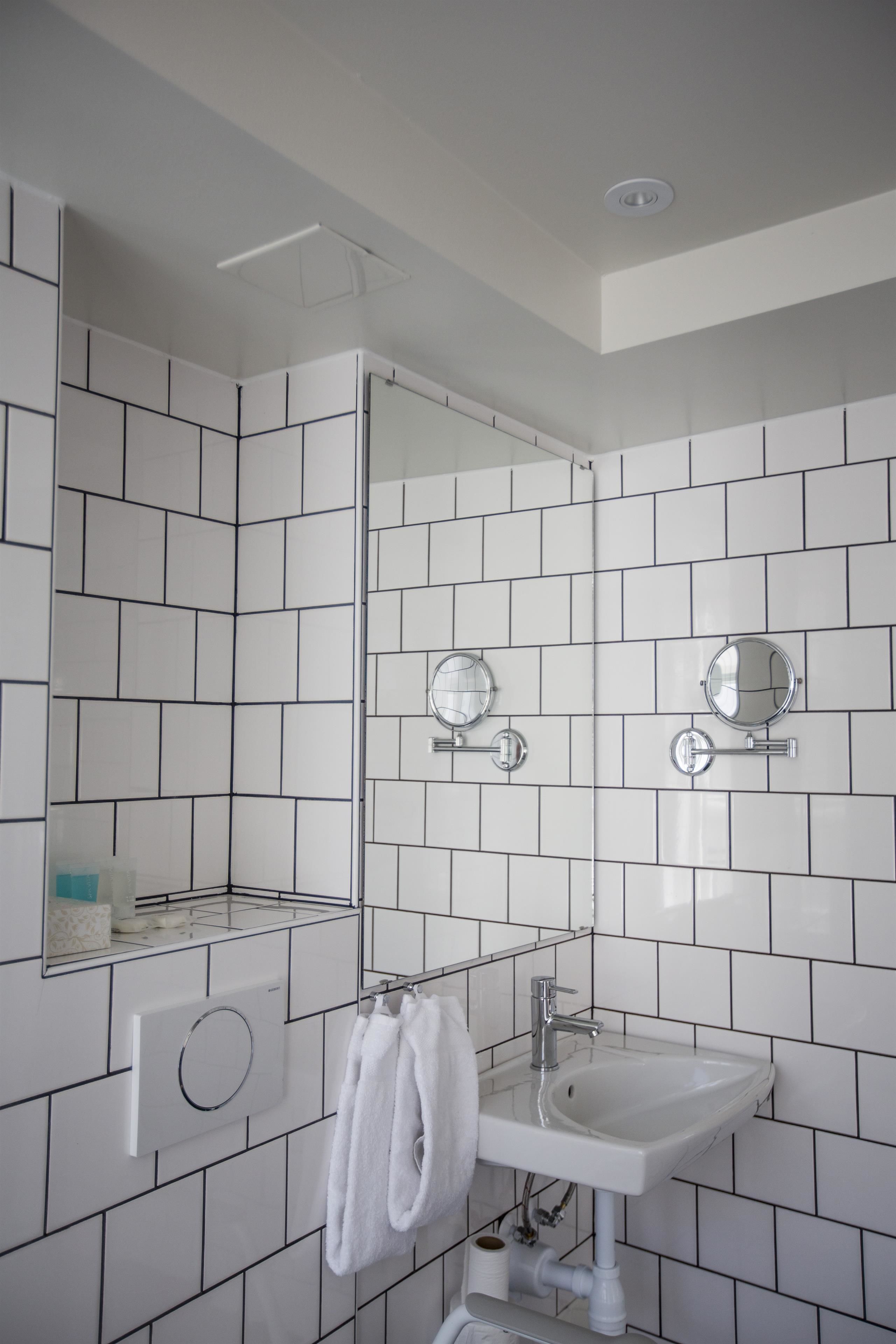 A modern bathroom with white tiles, a sink, a mirror, and a towel rack.