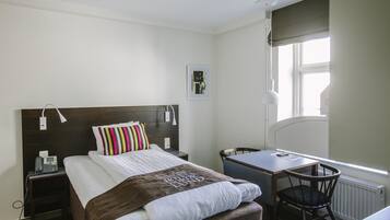 Ein Hotelzimmer mit Bett, Nachttisch, Stuhl, Schreibtisch und Fenster.