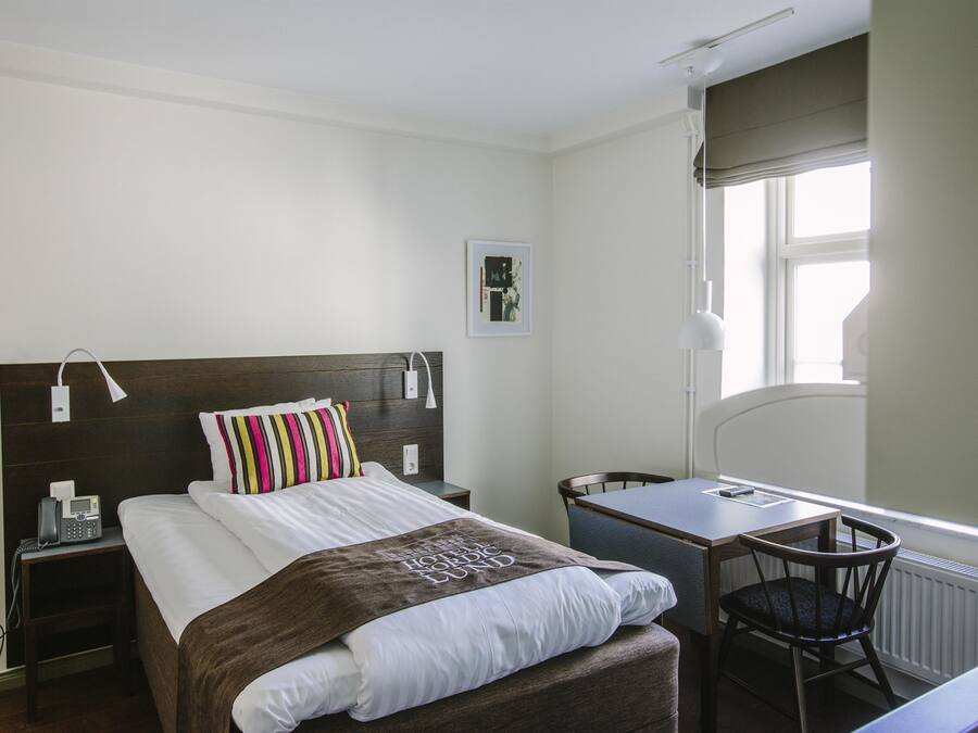Ein Hotelzimmer mit Bett, Nachttisch, Stuhl, Schreibtisch und Fenster.