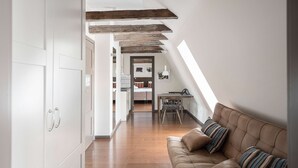 Un loft moderno con vigas de madera a la vista, un sofá de cuero marrón acogedor y un comedor con una mesa pequeña y sillas.