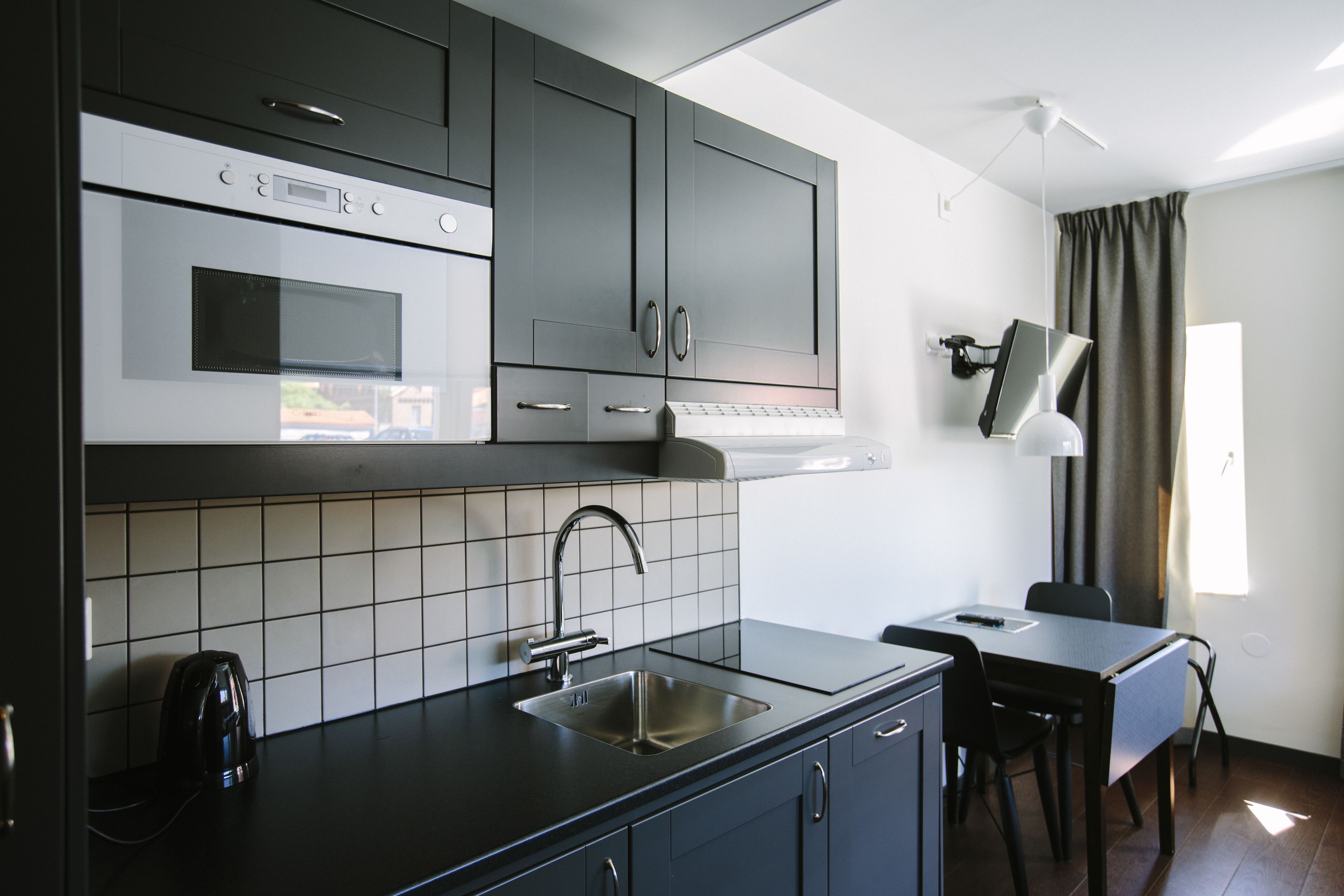 A modern kitchen with a built-in oven, microwave, and sink. There is a dining area with a table and chairs.