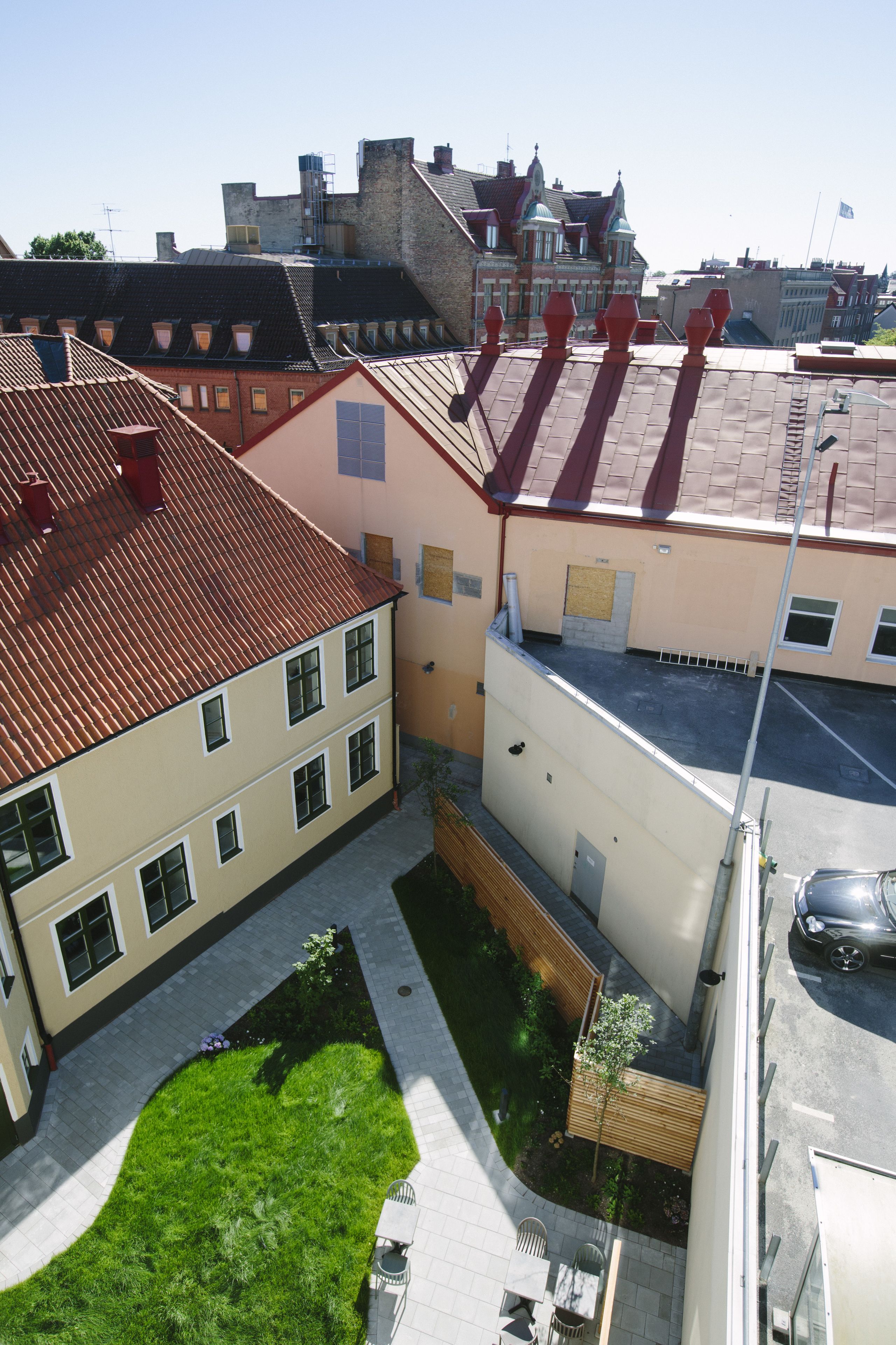 Um pátio com gramado, um espaço de estar pequeno e um edifício com telhado de telhas vermelhas.