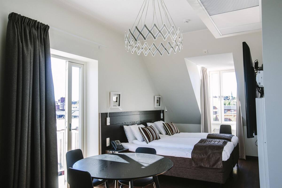 Quarto de hotel moderno com cama, uma mesa de jantar e vista para a cidade.