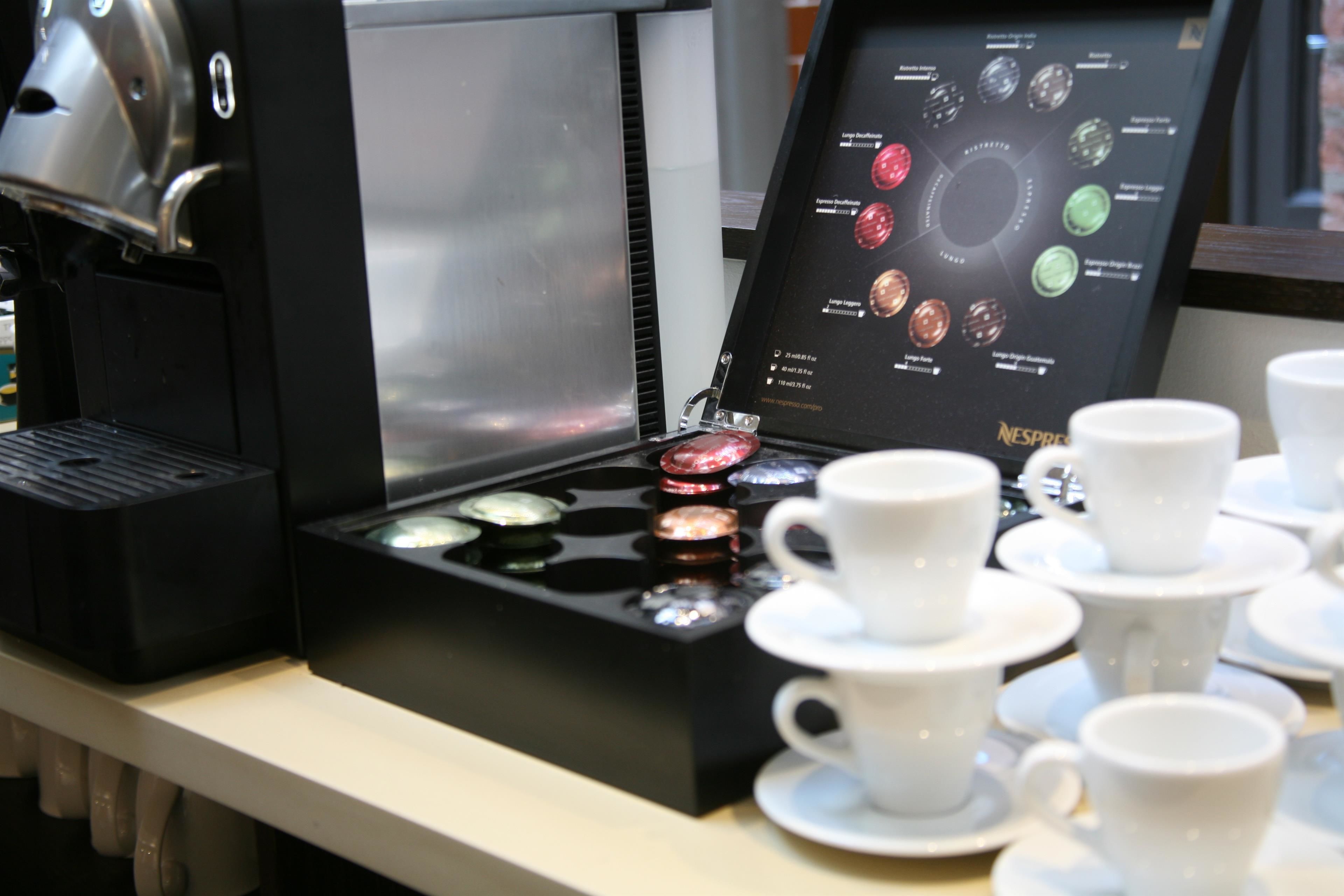 A coffee machine with a selection of coffee pods and several white cups and saucers on a counter.