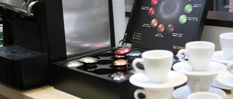 A coffee machine with a selection of coffee pods and several white cups and saucers on a counter.