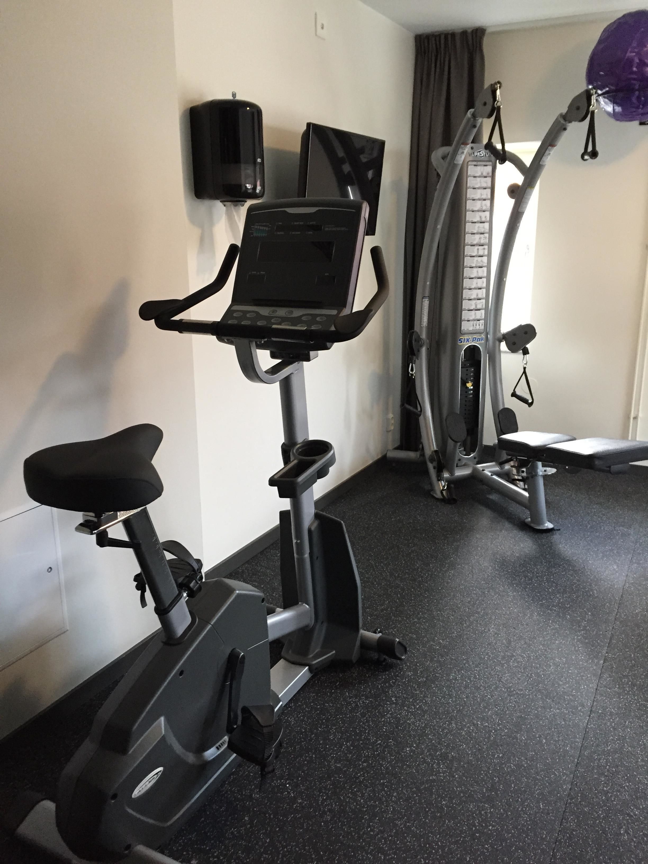 Ein Fitnessraum mit einem Ergometer, einem Laufband und einem an der Wand montierten Fernseher.