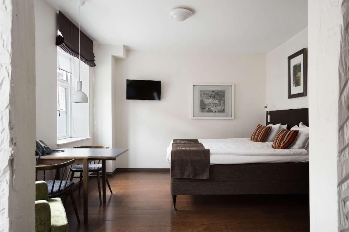 Una habitación con una cama, un escritorio, una silla, un televisor y un cuadro en la pared.
