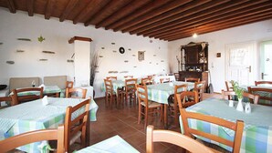 A dining area with wooden tables and chairs, a clock on the wall, and a wooden ceiling. - Cape Napos (Sifnos)