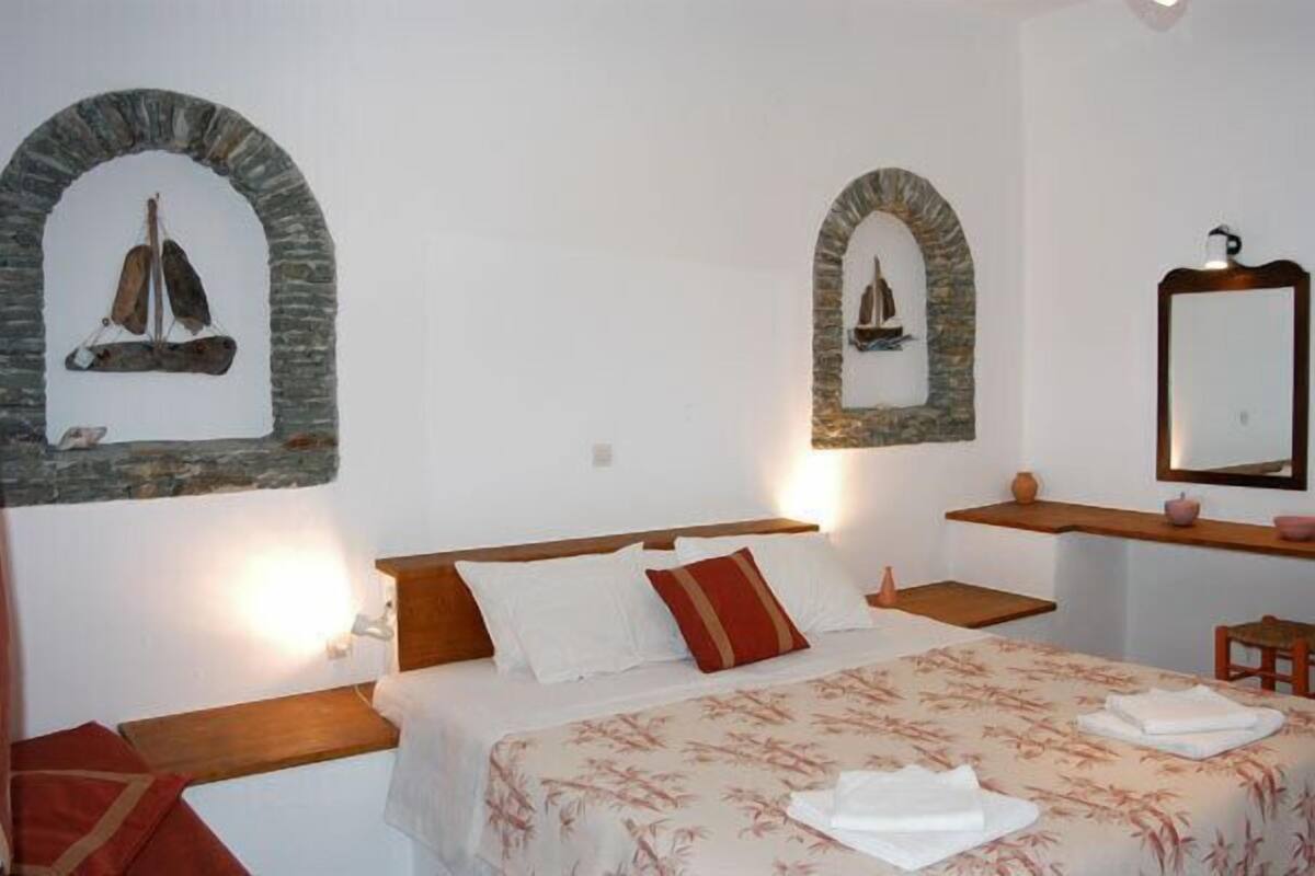 A bedroom with a bed, pillows, a nightstand, a mirror, and two wall-mounted shelves with decorative items.