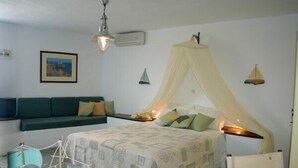 A bedroom with a bed under a canopy, a sofa, and a small table. - Cape Napos (Sifnos)