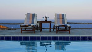 A poolside area with two lounge chairs and a table, overlooking a body of water. - Cape Napos (Sifnos)