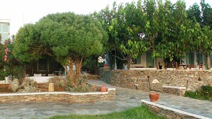 A stone patio with a grassy area, a tree, and a stone wall. - Cape Napos (Sifnos)