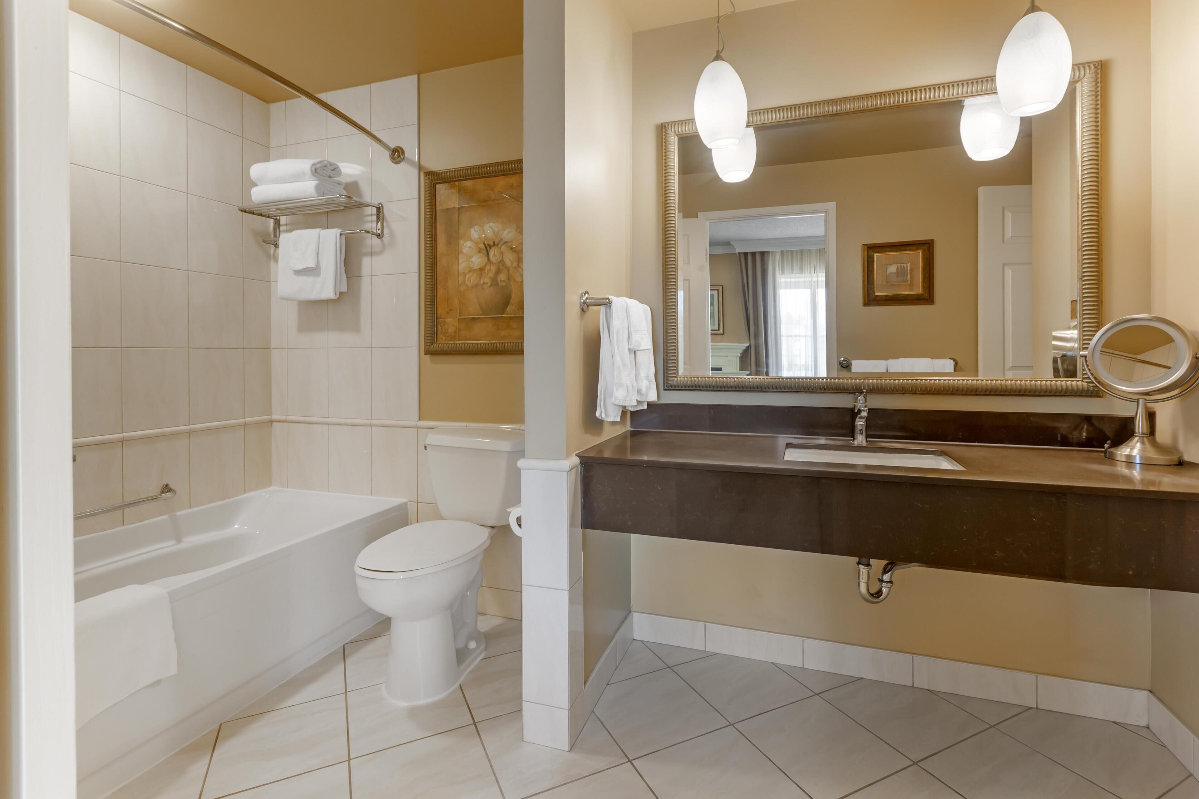 A modern bathroom with a bathtub, toilet, vanity, and large mirror.