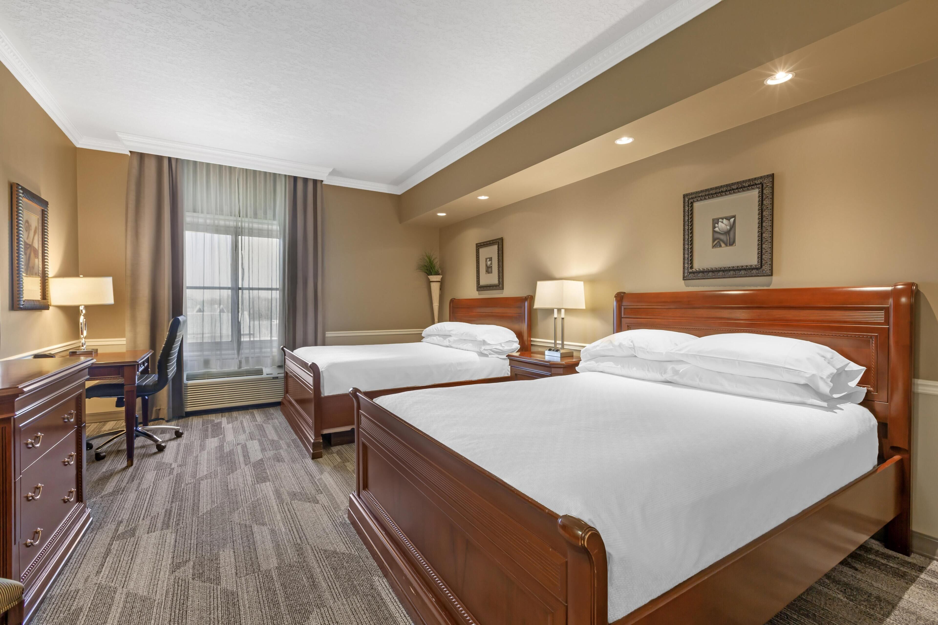 A hotel room with two beds, a desk, a chair, and a window with curtains.