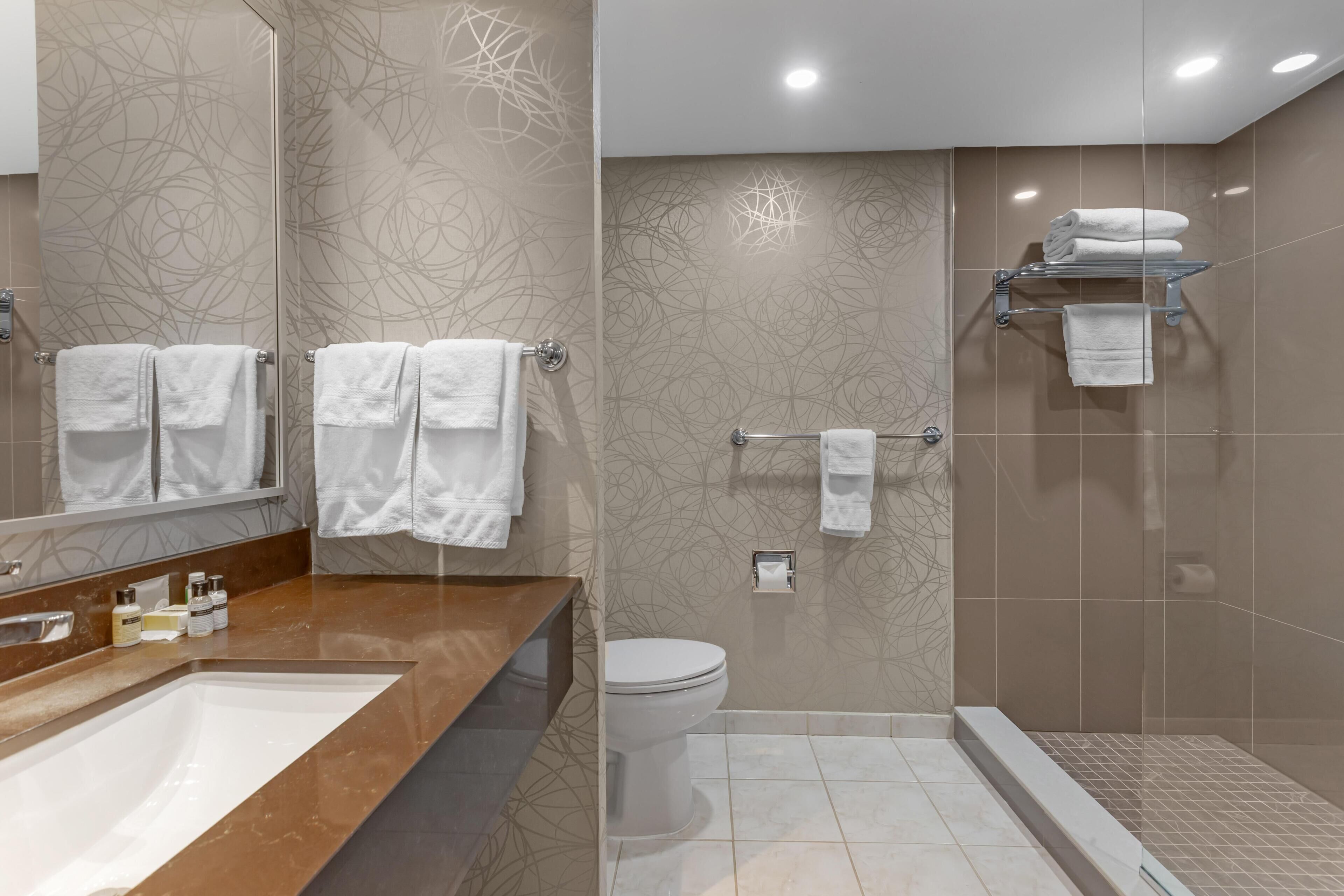 Ein modernes Badezimmer mit großem Spiegel, Waschbecken, Toilette und Duschbereich.