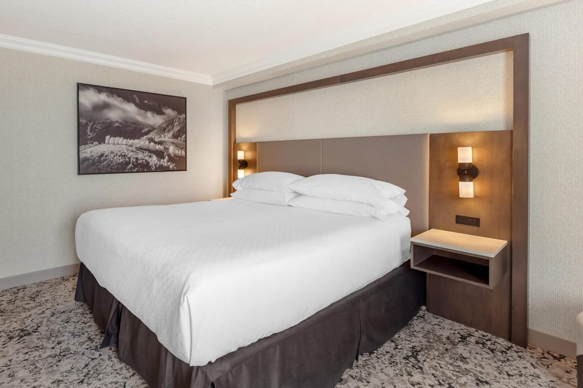 Una habitación de hotel con una cama grande, dos lámparas de noche, un estante pequeño y un cuadro en la pared.