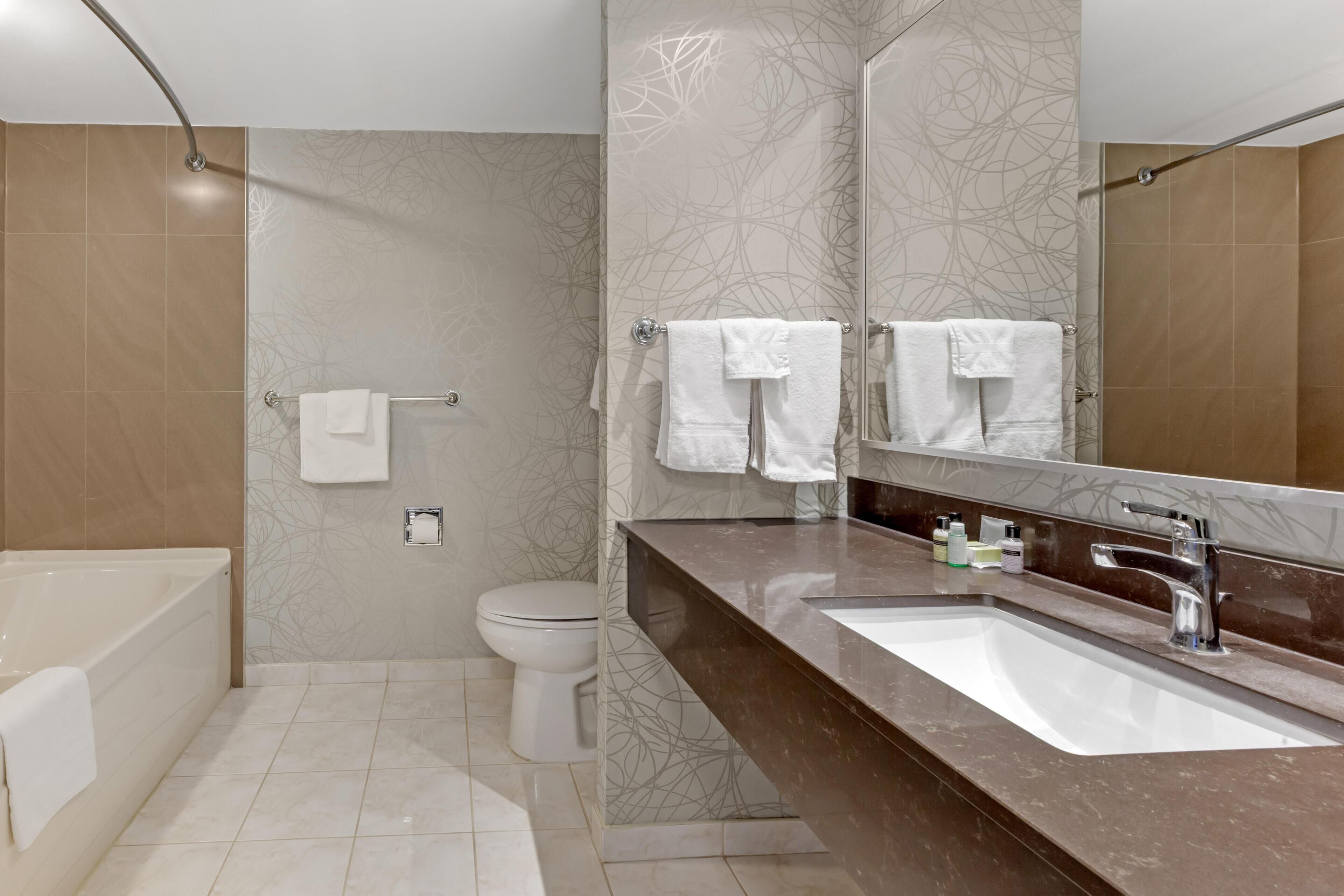 A modern bathroom with a bathtub, toilet, and a large mirror above the sink.