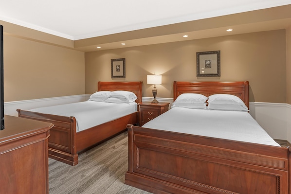A hotel room with two wooden beds, a nightstand with a lamp, and a dresser.
