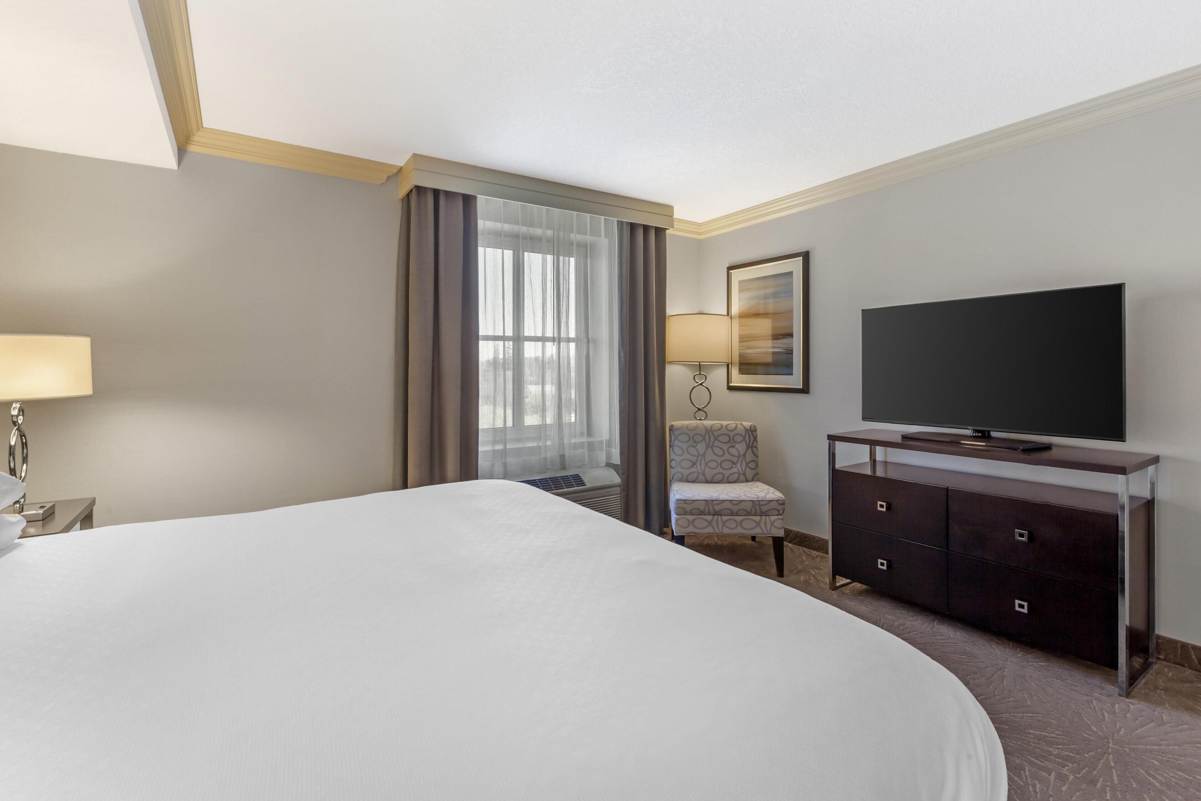 A hotel room with a large bed, a flat-screen TV, a desk with a lamp, and a chair.