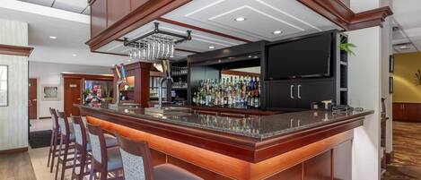 A bar area with a long counter, bar stools, a television, and a variety of bottles.