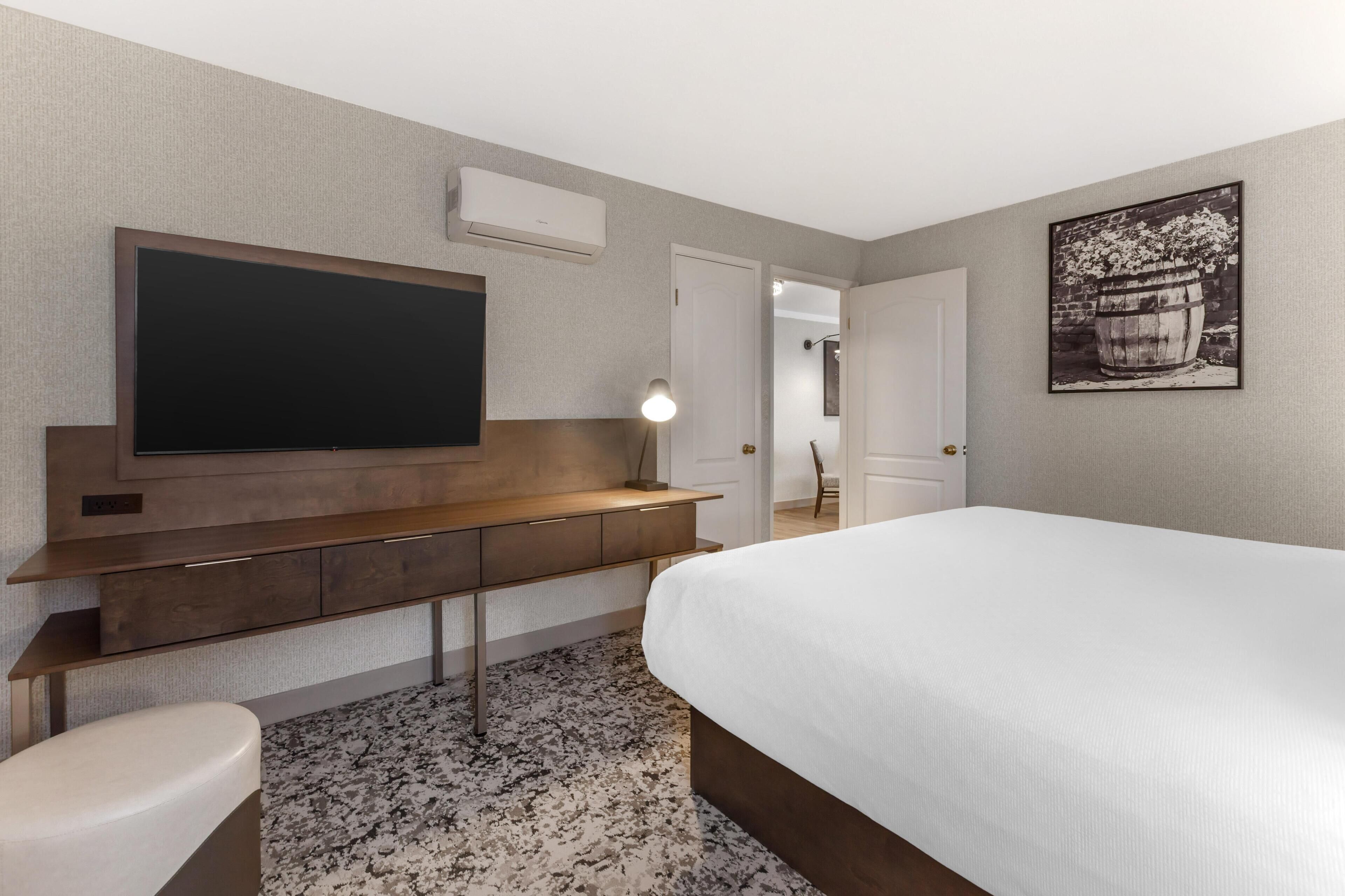 Una camera d'albergo con un letto, una scrivania con televisore a schermo piatto, una lampada e un quadro appeso al muro.