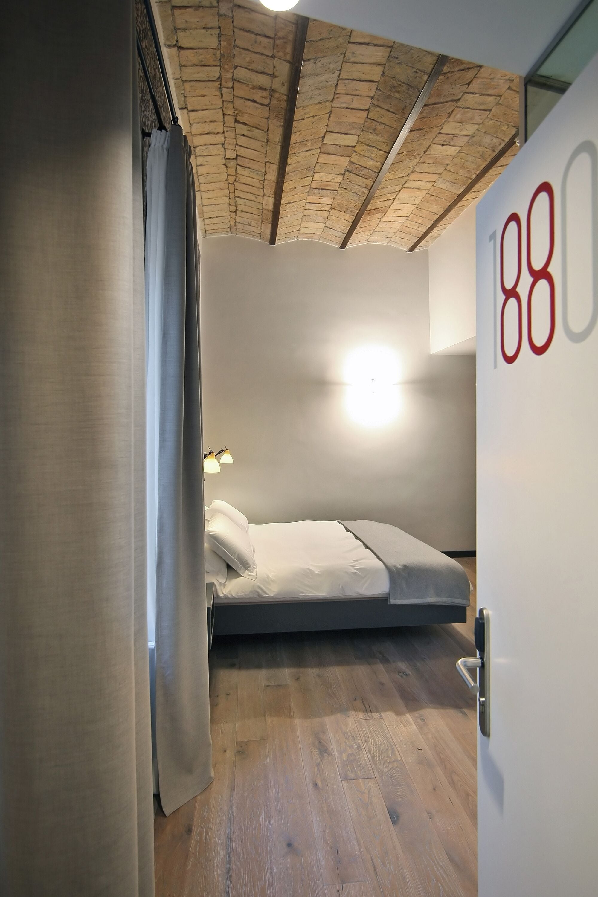A room with a bed, a number '88' on the wall, and a ceiling with exposed brickwork.
