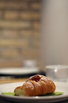 A croissant on a white plate with a green leaf underneath, set on a table with a blurred background.