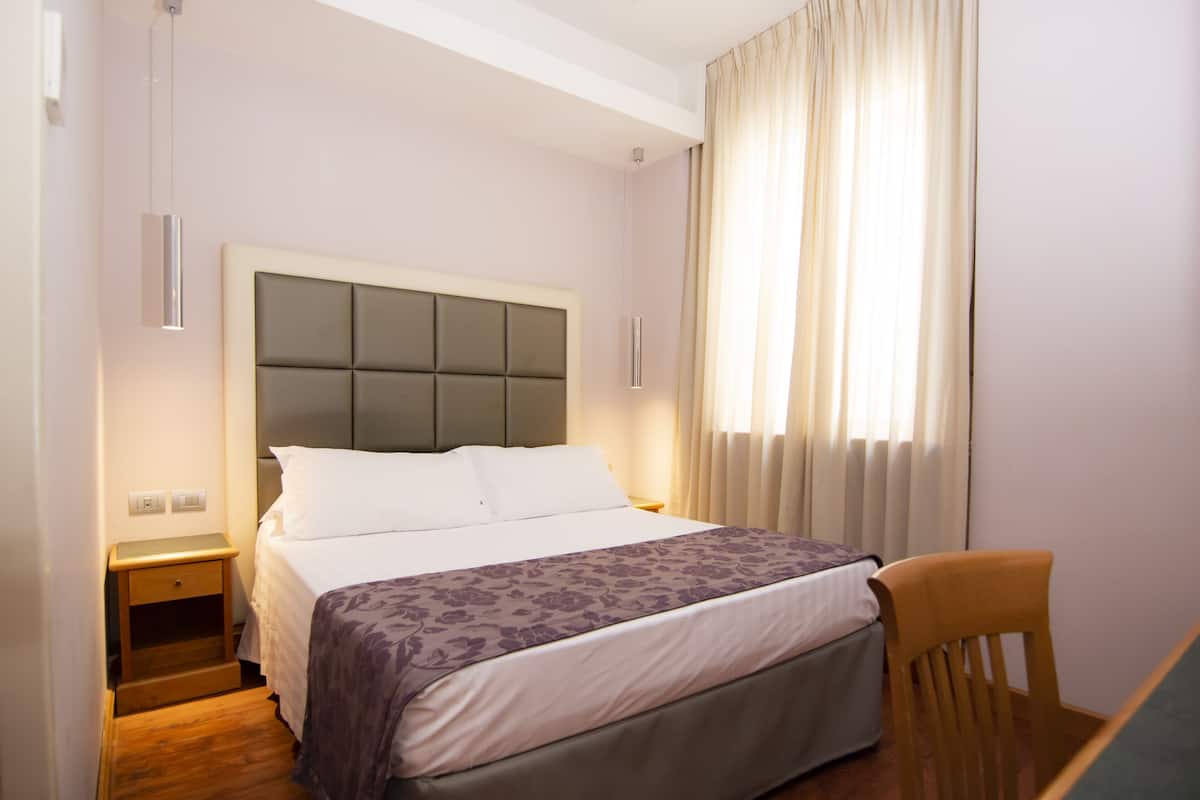 A bedroom with a bed, a nightstand, a chair, and a window with curtains.