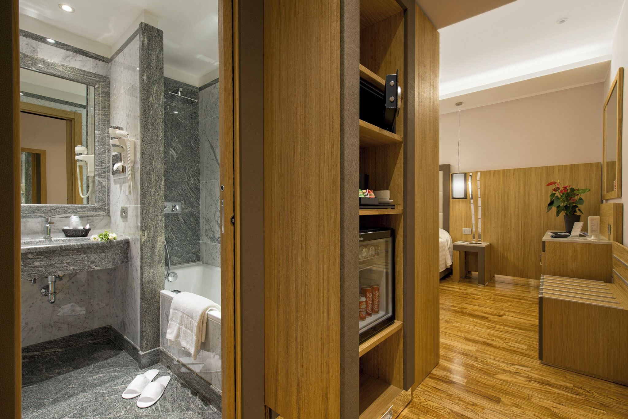 Un baño moderno con un lavabo de mármol, mampara de ducha de vidrio y tocador de madera con refrigerador.