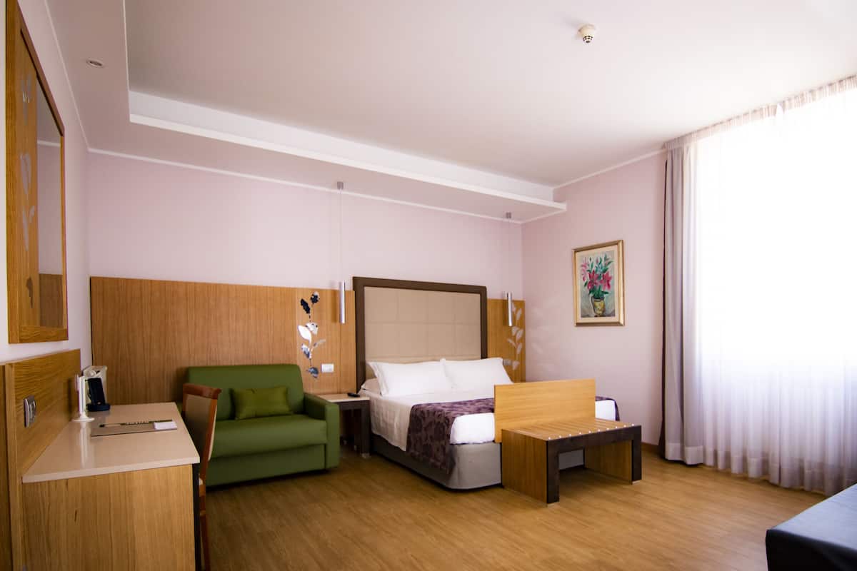 A hotel room with a bed, a green sofa, a wooden desk, and a small table.