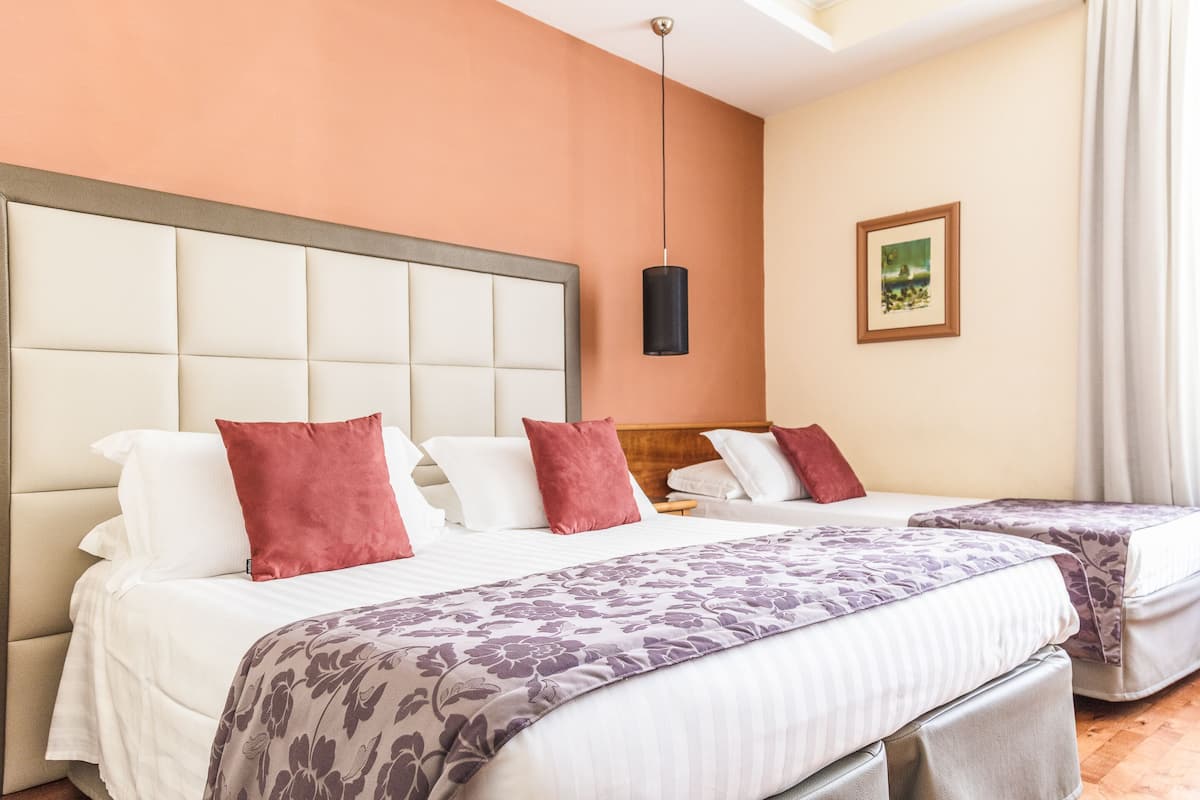A hotel room with two beds, a headboard, a hanging light fixture, and a framed picture on the wall.
