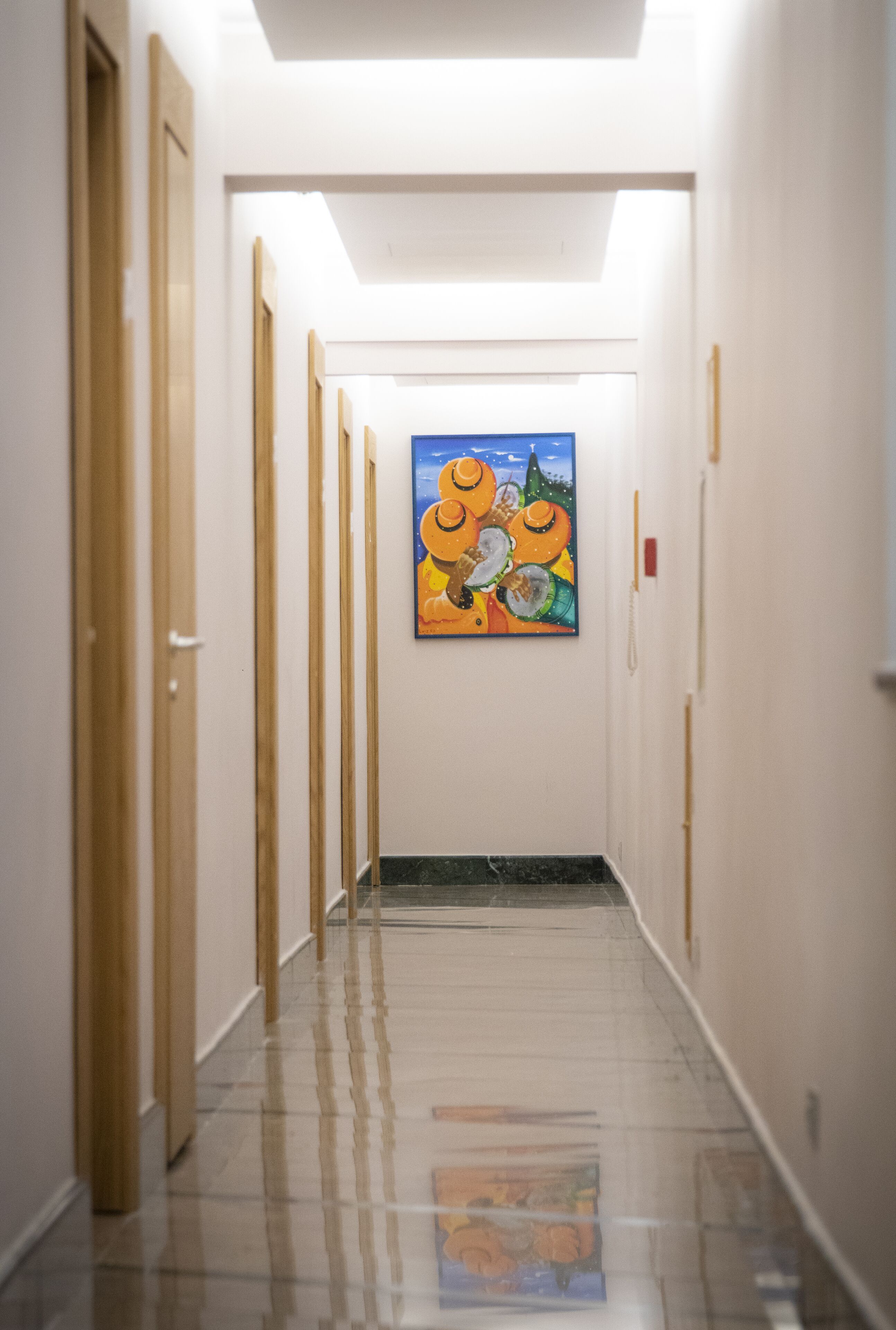A hallway with wooden doors and a tiled floor leading to a room with a painting.