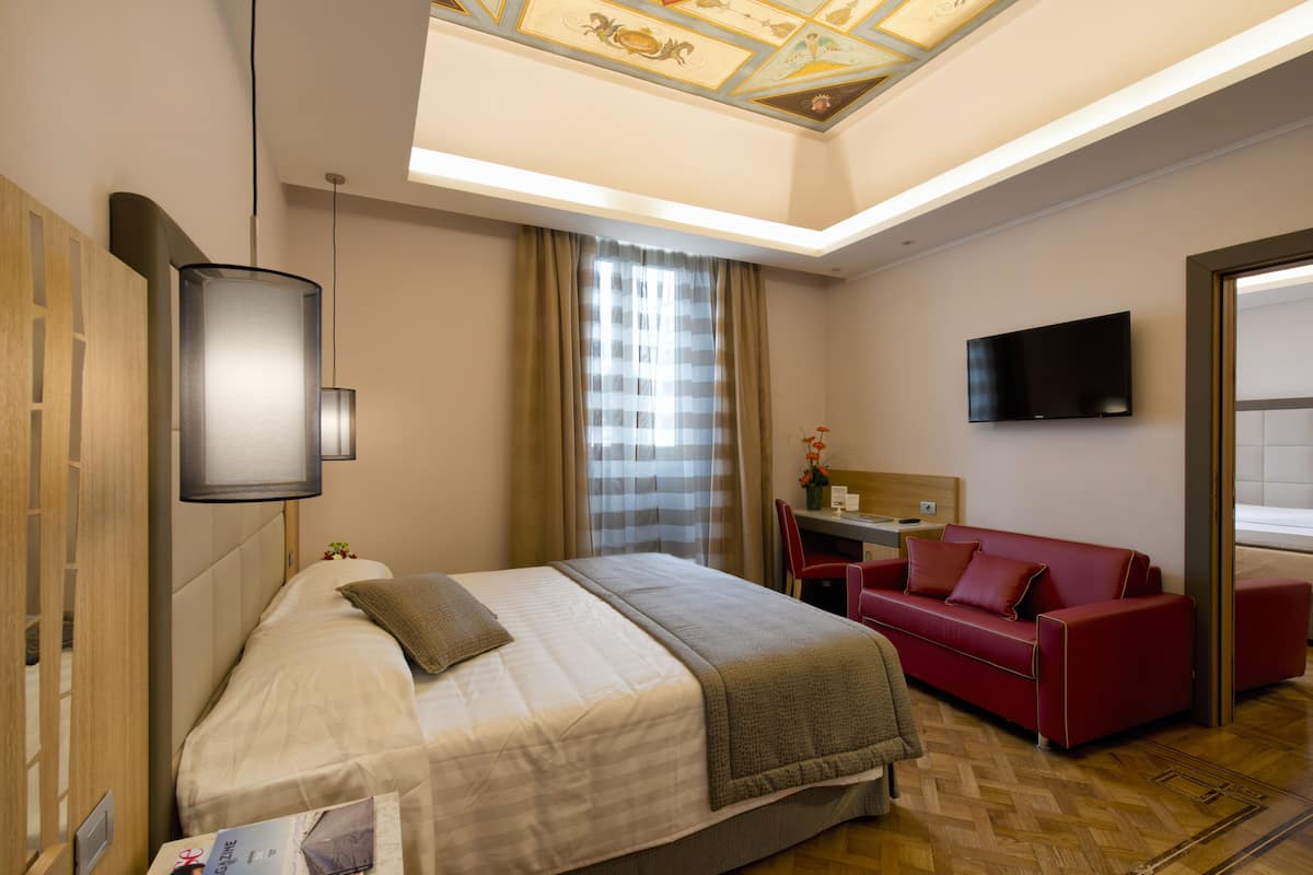 A hotel room with a bed, a red sofa, a TV, and a ceiling with a decorative design.
