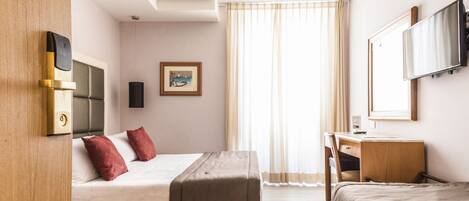 A hotel room with a bed, a desk, a chair, a television, and a window with curtains.