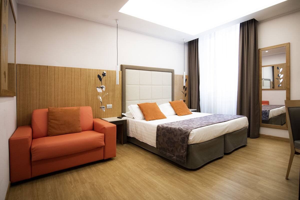 A hotel room with a bed, a sofa, a desk, and a mirror.