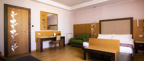 Habitación de hotel con un escritorio de madera, un sillón verde, una cama con cabecera de madera y un espejo grande en la pared.