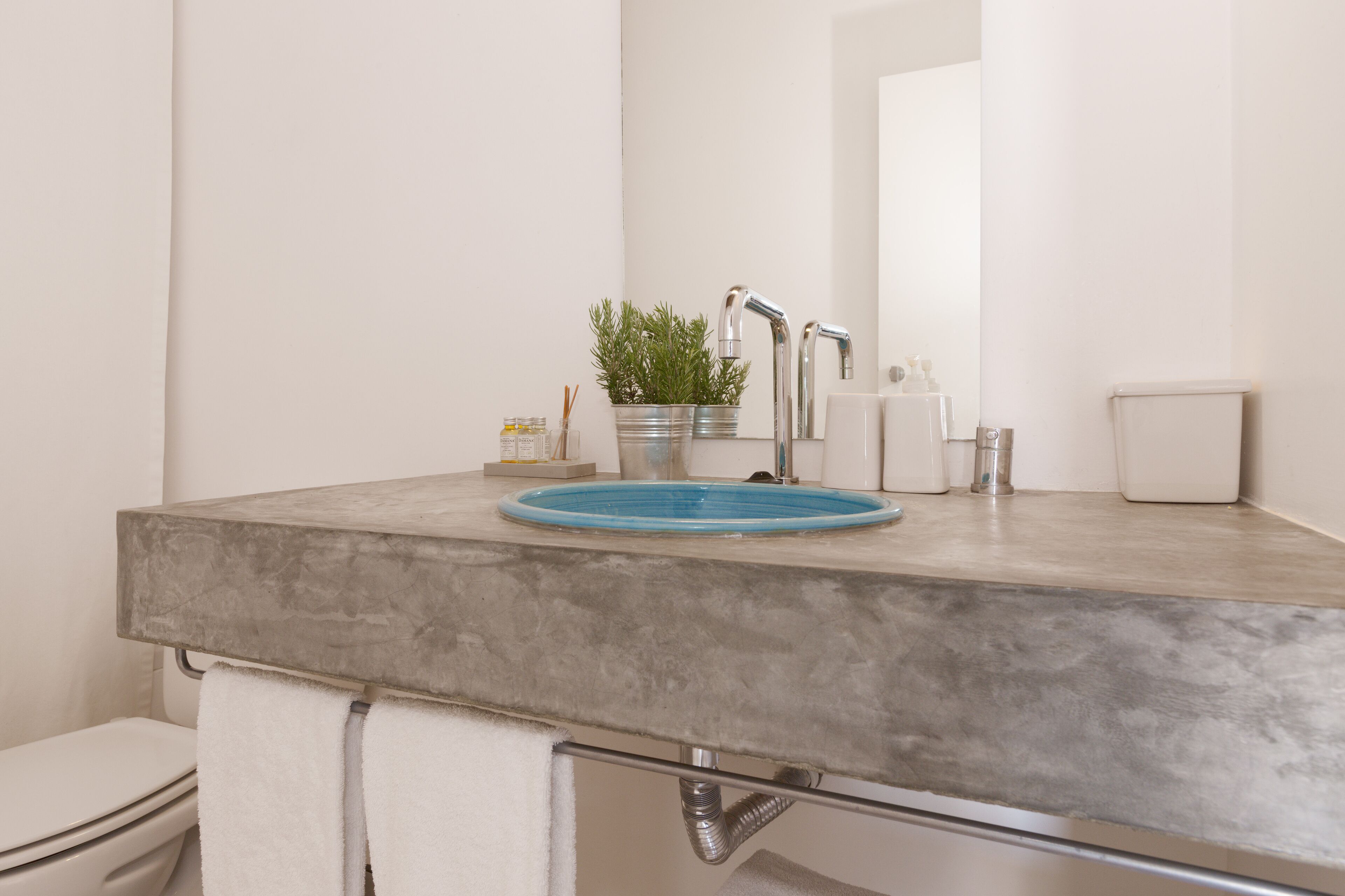 Un baño con encimera gris, lavamanos azul, inodoro blanco y espejo.
