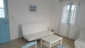Una habitación con un sofá blanco, una mesita, dos sillas, un cuadro en la pared y una puerta con cortina.