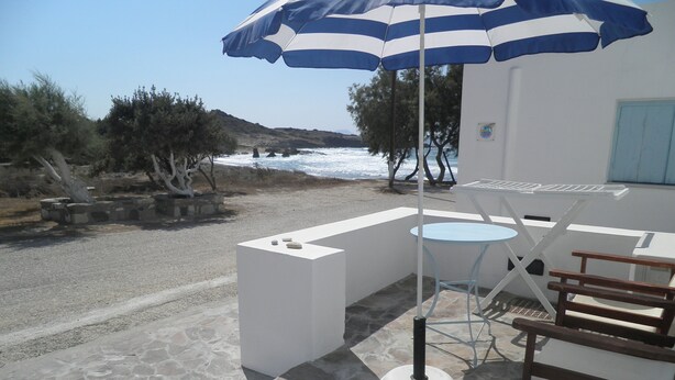 Una terraza con una mesa y sillas, un paraguas a rayas y vista al mar.