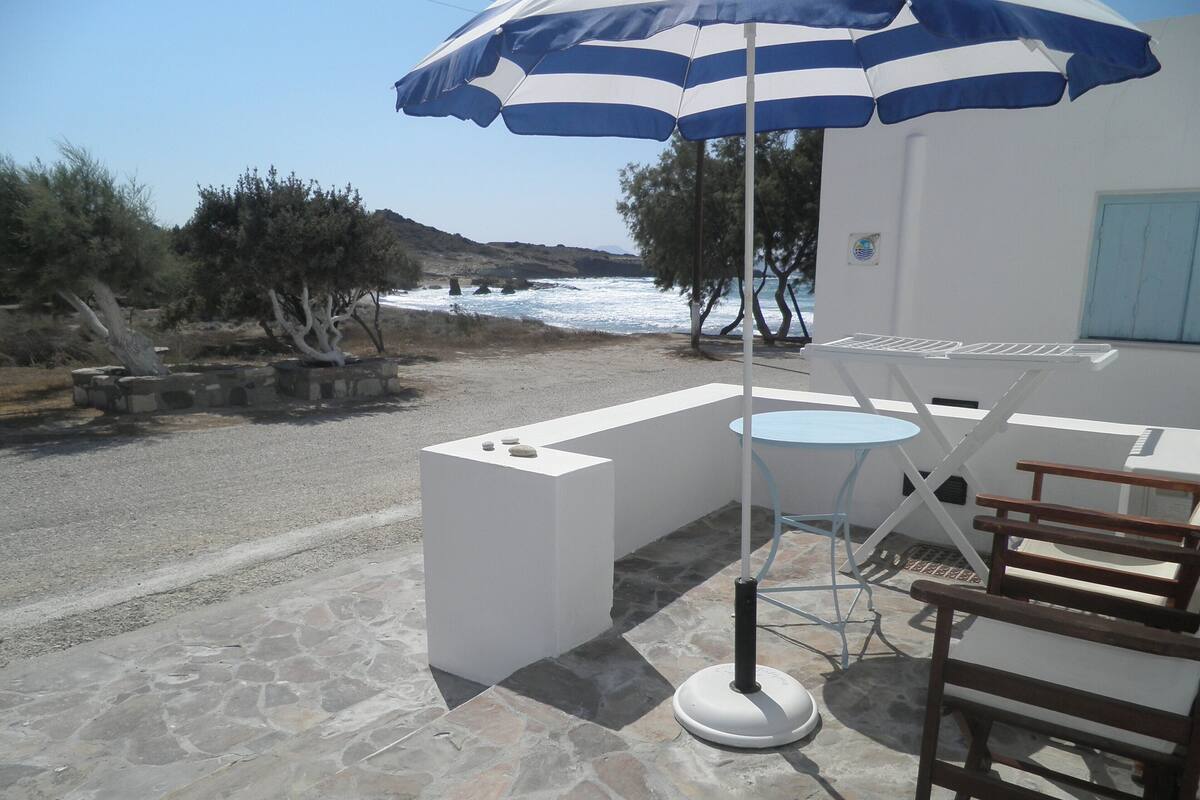 En terrass med ett bord och stolar, ett randigt parasoll och utsikt över havet.