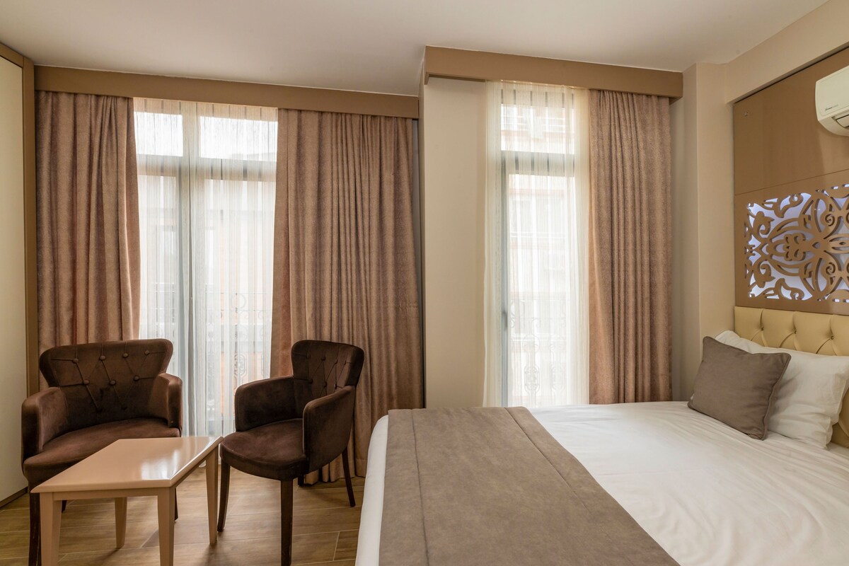 Ett hotellrum med en stor säng, två fåtöljer, ett litet bord och en dekorativ sänggavel.