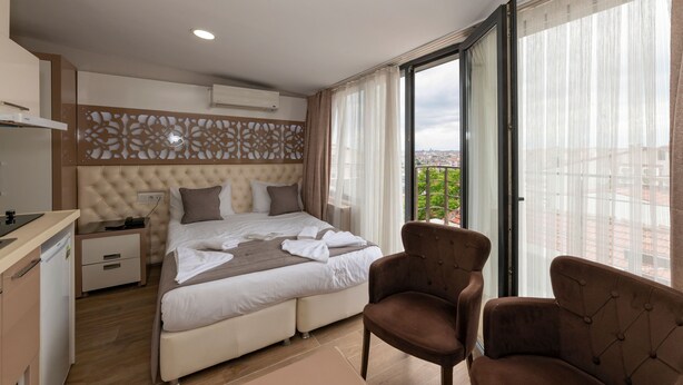 Une chambre d’hôtel moderne, dotée d’un grand lit, d’un bureau et d’une chaise. La chambre offre une vue sur la ville grâce à de grandes fenêtres.