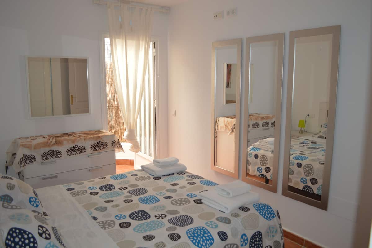 Habitación de hotel con cama, cómoda, espejo y ventana con cortinas.